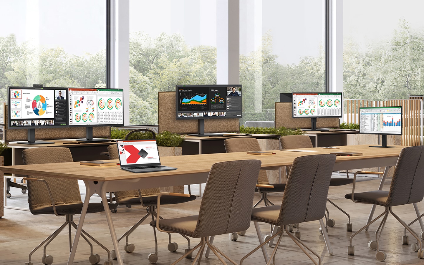 Shared office space with multiple desks, monitors, and a laptop displaying business presentations and charts