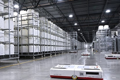 Automated warehouse with self-driving robots transporting white storage containers on polished floor.