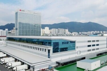 LG headquarters building with glass facade next to factory facility, mountains and city apartments in background