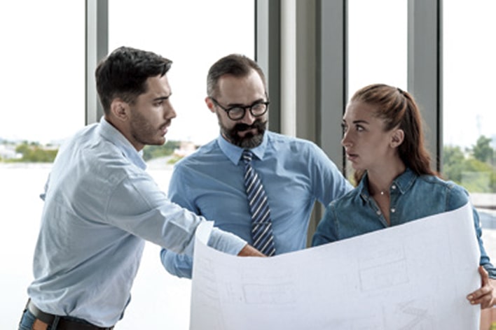 Business consultants reviewing architectural blueprints during LG engineering master plan and roadmap meeting for industrial projects.