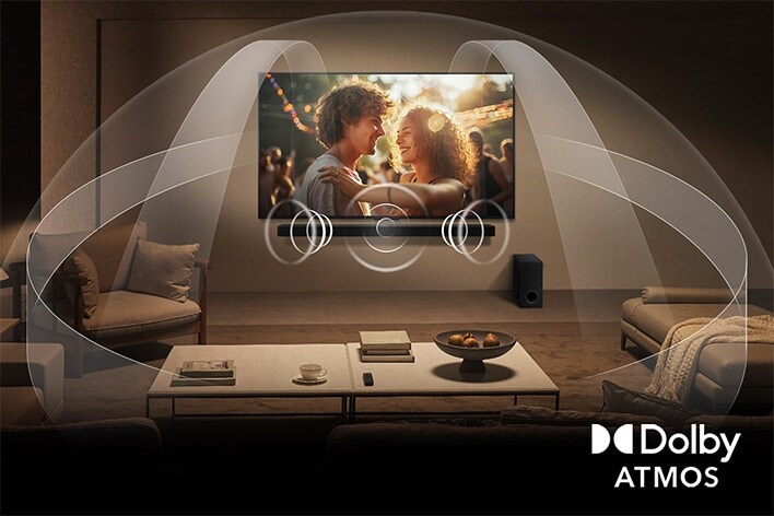Ruangan tamu yang remang-remang dan nyaman dengan TV LG QNED di dinding dan soundbar LG. Grafik menunjukkan bagaimana Dolby Atmos mengisi seluruh ruang dengan suara surround dari segala arah. Logo Dolby Atmos berada di pojok kanan bawah.