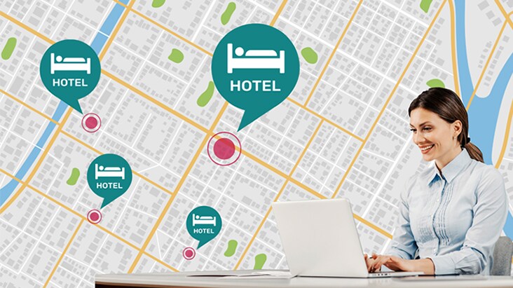 Seorang perempuan yang duduk di meja sedang menggunakan laptop-nya untuk mengelola TV hotel di berbagai lokasi yang berbeda.