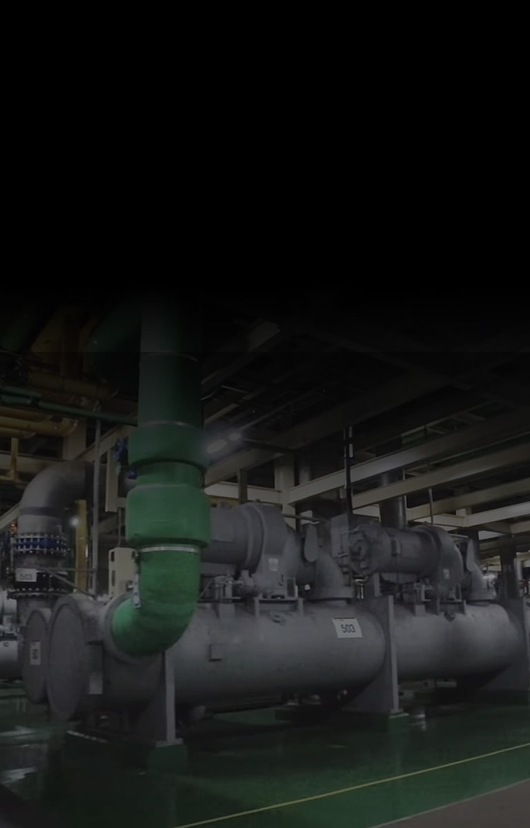 Unit LG Chiller berwarna abu-abu yang besar menarik perhatian di ruangan yang penuh mesin, kehadirannya semakin menonjol dengan pipa hijau/biru.