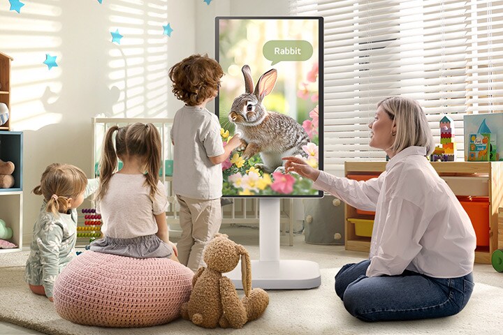 Gambar ini menunjukkan seorang wanita dan tiga anak bermain menggunakan LG Smart Monitor Swing.
