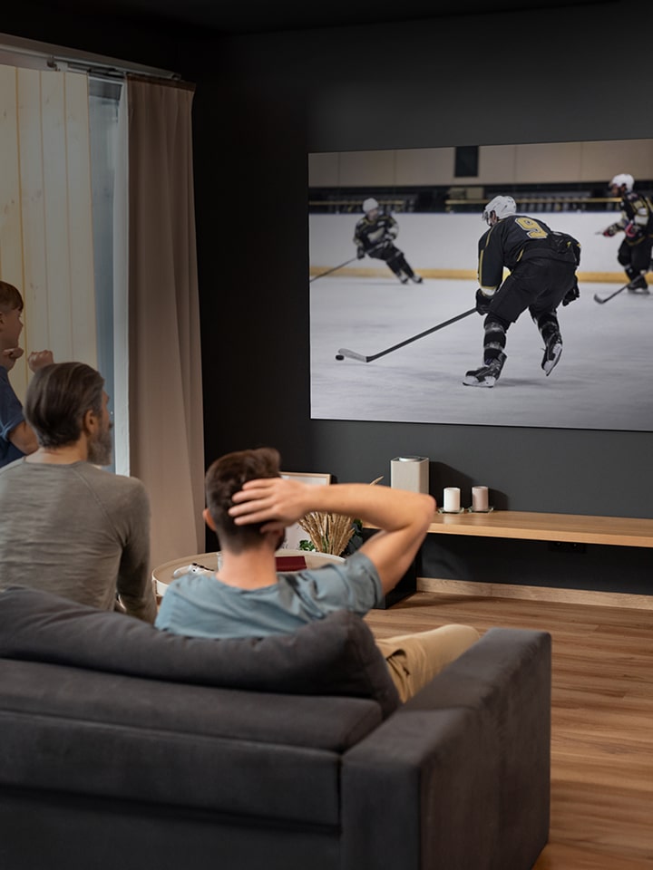 People sitting in a living room watching an ice hockey game on a large wall-mounted TV screen.