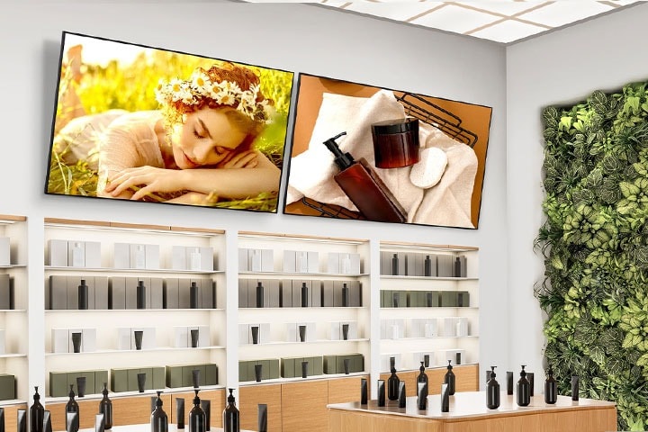 Inside the cosmetics shop, two signage displays are mounted high on the wall with a downward tilt, each vividly showcasing cosmetic advertisements.