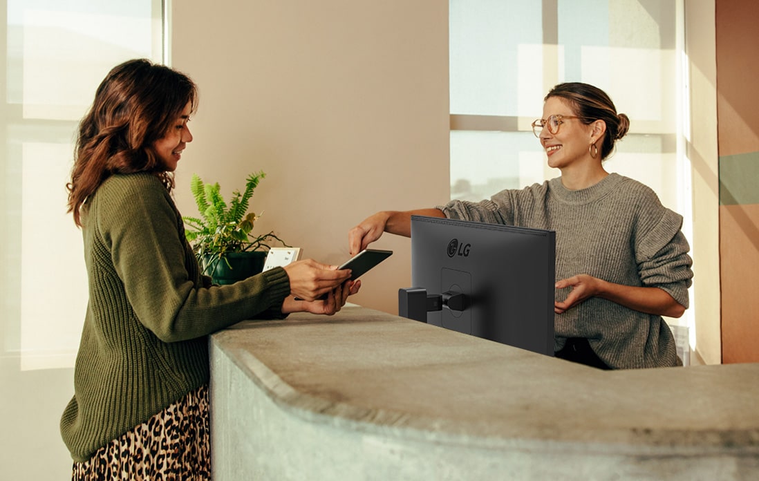Friendly receptionist showing a woman where to sign on a digital tablet.	