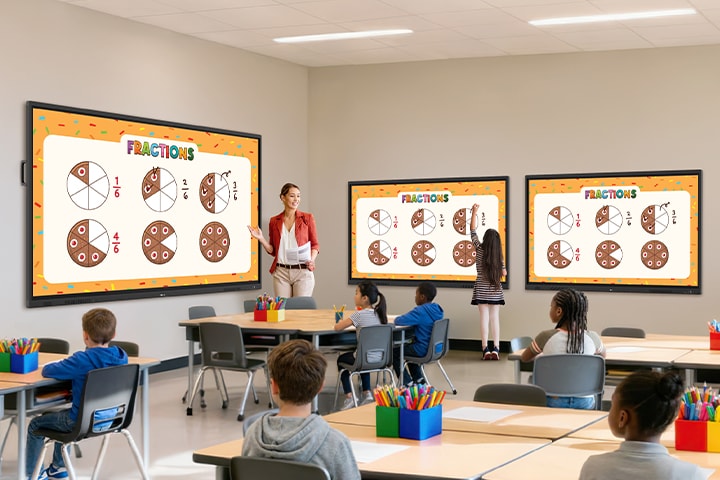 Multiple TR3ER are installed in a classroom to display learning content as a teacher conducts a lesson. One student is directly writing on a TR3ER, participating in the class.