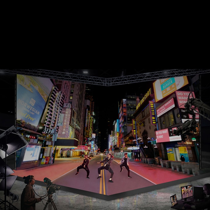 Configuración de estudio con una gran pantalla LED curva que muestra una vibrante escena de una calle de la ciudad por la noche. Artistas bailan frente a la pantalla mientras un camarógrafo graba, simulando un entorno urbano al aire libre en interiores.