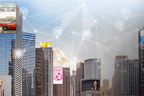 Horizonte de una ciudad con edificios altos que presentan grandes carteleras digitales. Los gráficos superpuestos muestran íconos de red interconectados, que simbolizan la conectividad de una ciudad inteligente y la comunicación digital.