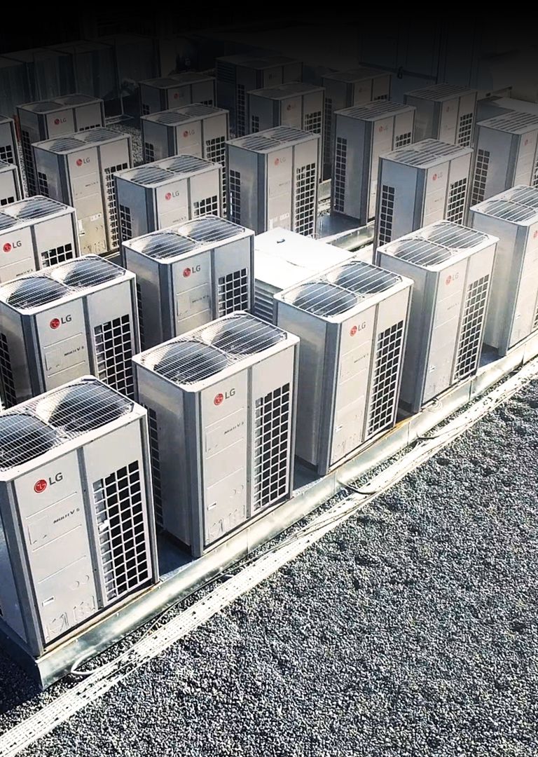 "Vista aérea de una serie de unidades LG Multi V i, con la mitad derecha cubierta por conductos de ventilación cuadriculados, alineadas en el techo del edificio. "