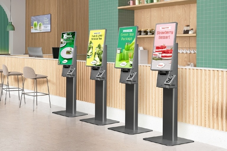 Hay cuatro quioscos LG colocados uno al lado del otro en una cafetería, cada uno de los cuales muestra diferentes anuncios de menús en sus pantallas en modo de espera.
