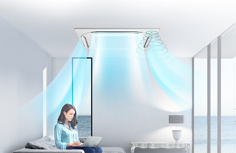 A woman, laptop in hand, sits on a sofa under the LG Ceiling-mounted cassette, blowing airflow into the room with the ocean view.