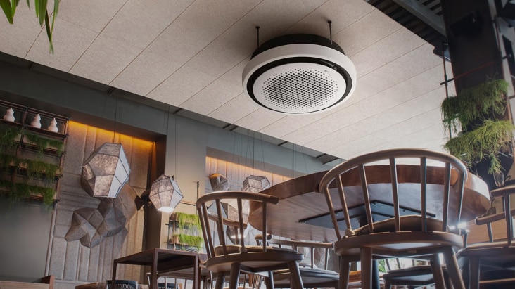 LG Ceiling Mounted Cassette, montado no teto, num espaço comercial moderno. Proporciona refrigeração discreta, integrando-se com elegância no design de interiores.