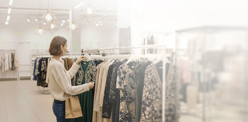 امرأة تتسوق في متجر للأزياء، تحمل فستانًا أخضر اللون مطرَّزًا وحقيبة تسوق.