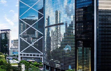 Modern glass skyscrapers in a city business district reflecting sunlight and surrounding buildings.