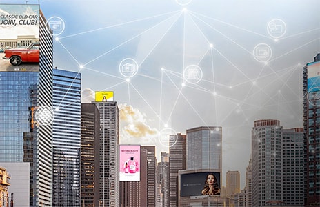 أفق المدينة مع مباني شاهقة تضم لوحات إعلانية رقمية كبيرة. رسومات متراكبة تُظهر أيقونات شبكة مترابطة، ترمز إلى اتصال المدن الذكية والاتصالات الرقمية