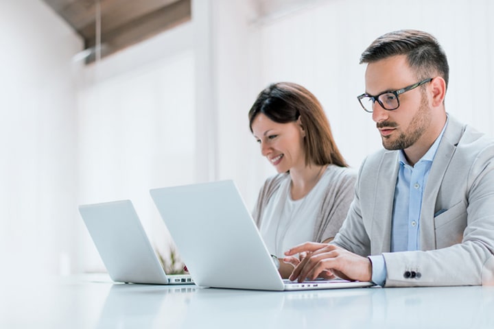 Two administrators are managing devices using LG SuperSign Control+ on personal PCs.