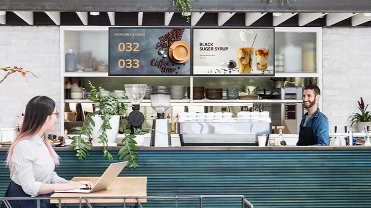 The cafĂŠ's queue display shows completed food numbers, with a customer checking the information.