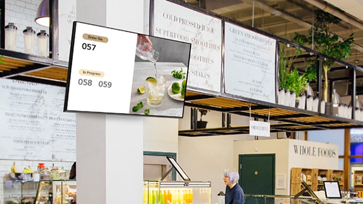 A signage screen mounted on a store wall displays menu images and related information.