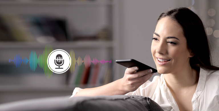 A woman is controlling TV by speaking to a remote control which has voice recognition.
