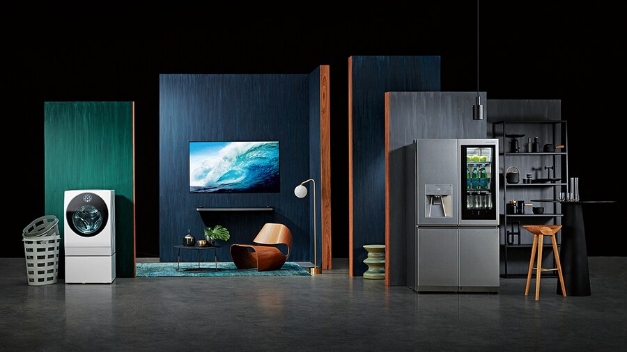 starting from the left, lg signature washing machine, oled tv w, refigerator is displayed with some green and blue wall in some place like a dark studio