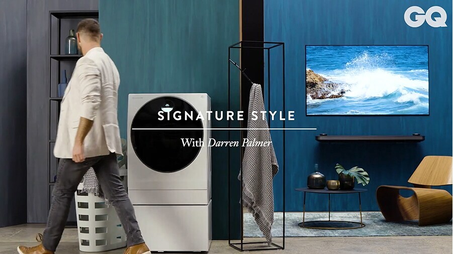 darren palmer is walking by lg signature washing machine which is laid in the overall blue colored living room with lg signature oled tv w on the right side