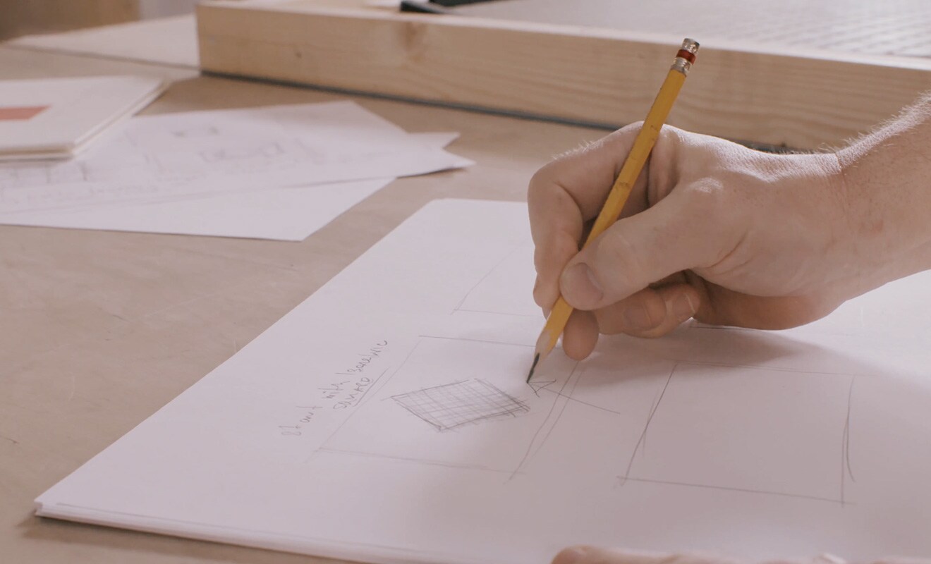 Matt Clark's hand is holding a pencil and drawing something on a paper