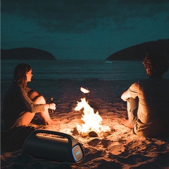 Pessoas na praia a noite com fogueira e caixa XBOOM Go XG9