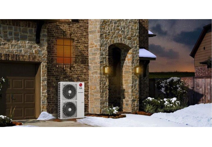 Texto alternativo: Um sistema de aquecimento por bomba de calor da LG do lado externo de uma casa de pedra em um ambiente com neve, demonstrando a capacidade de manter o aquecimento em um clima frio.