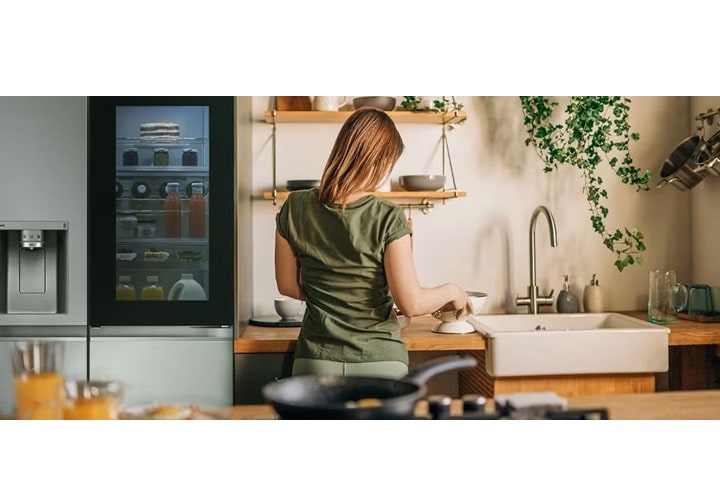Uma pessoa está organizando itens em uma superfície plana em uma cozinha com decoração de madeira. Há uma geladeira ao lado dela.