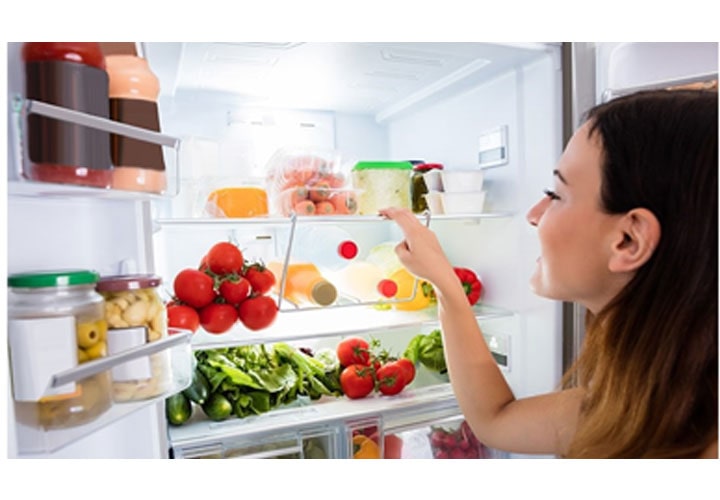 Uma mulher olha dentro de uma geladeira cheia de vegetais e frutas.