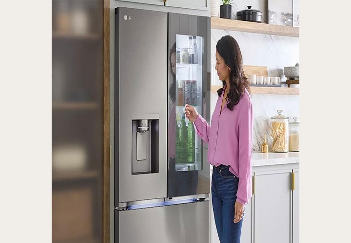 Mulher interage com geladeira LG French Door em aço inox com InstaView, acessando bebidas e itens frequentes; dispenser na porta esquerda.