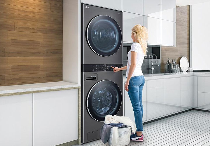 Texto alternativo: Uma mulher usa uma WashTower™ LG em uma cozinha moderna, demonstrando o design que economiza espaço e cuida das roupas com eficiência.