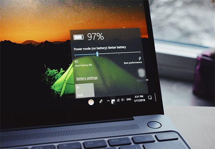 A tela de um laptop mostra o status da bateria com 97% e opções de carregamento, com um papel de parede de pôr do sol.