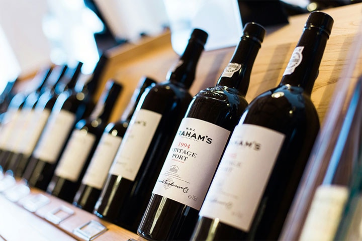 Close de uma fileira de garrafas de vinho em exposição, contra um fundo desfocado em uma loja de vinhos ou sala de degustação.