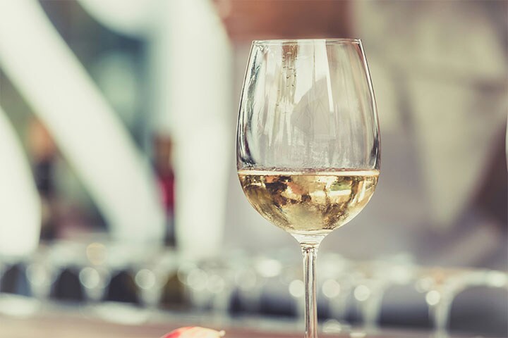 Close de uma taça de vinho branco sobre uma mesa com fundo desfocado, destacando as taças elegantes e o vinho espumante dentro.