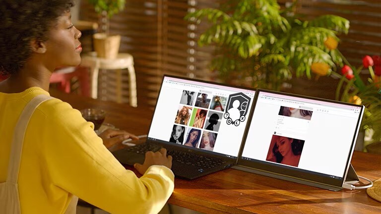 Mulher trabalhando em um laptop LG de tela dupla em uma mesa com plantas ao fundo.