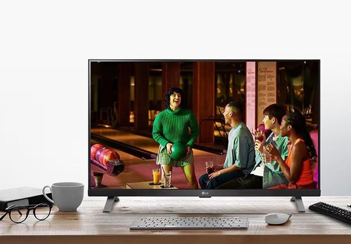 Monitor LG de baixo custo exibe uma cena de reunião entre amigos, destacando cores vibrantes e imagens nítidas, ideais para assistir a conteúdo de entretenimento.