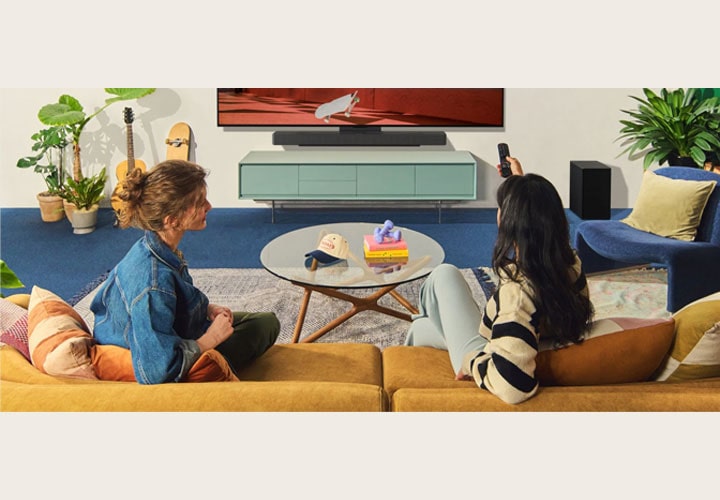Duas pessoas assistem a um filme em uma sala moderna com Smart TV LG e soundbar, criando uma experiência de entretenimento envolvente.
