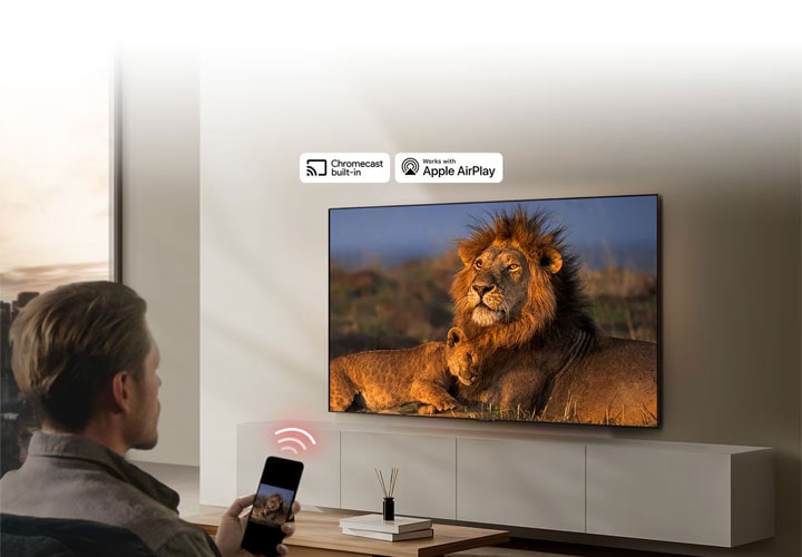 Homem utiliza smartphone para transmitir conteúdo para uma Smart TV LG com suporte para Chromecast e Apple AirPlay, exibindo uma cena de leões.