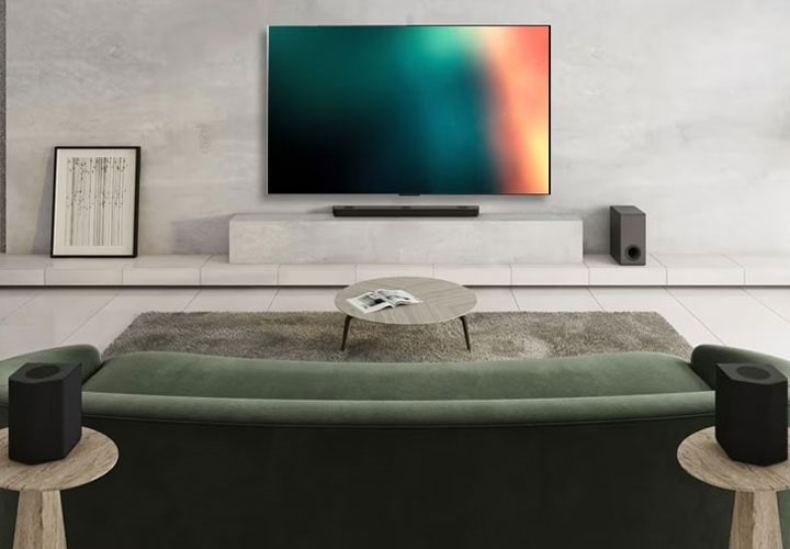Sala de estar moderna com TV de tela plana montada na parede, uma barra de som elegante abaixo, um sofá verde, uma mesa de centro redonda e alto-falantes surround de cada lado.
