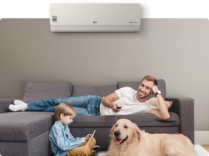 Pai e filho relaxam no sofá com um cachorro dourado ao lado, sob um ar-condicionado LG Dual Inverter na parede.