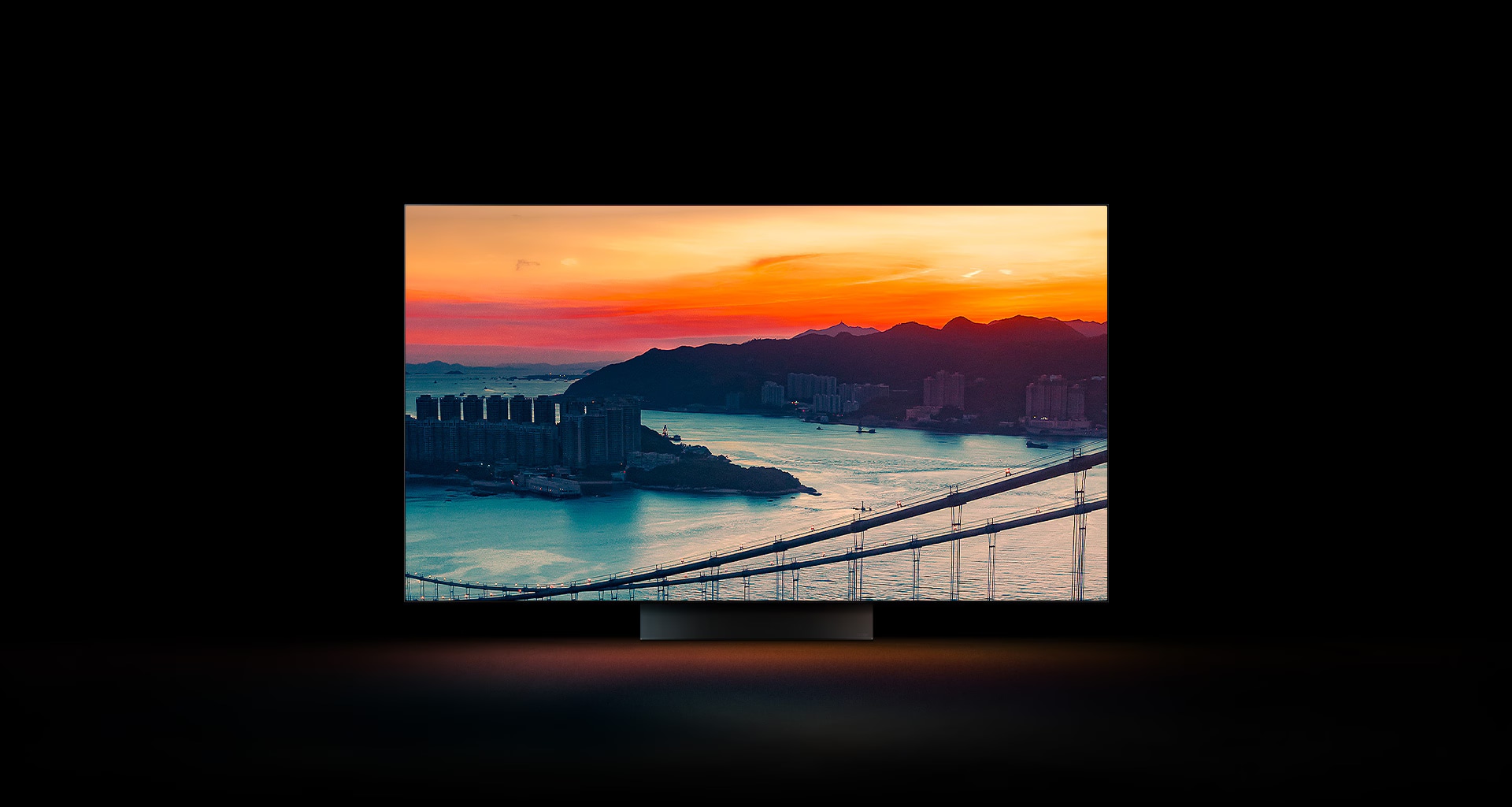 Die Luftaufnahme einer Küstenstadt mit Verkehr auf einer Brücke bei Sonnenuntergang erscheint auf dem gesamten Display. Sie wird beschnitten und auf einem LG OLED-Fernseher mit unveränderten Originalfarben angezeigt.