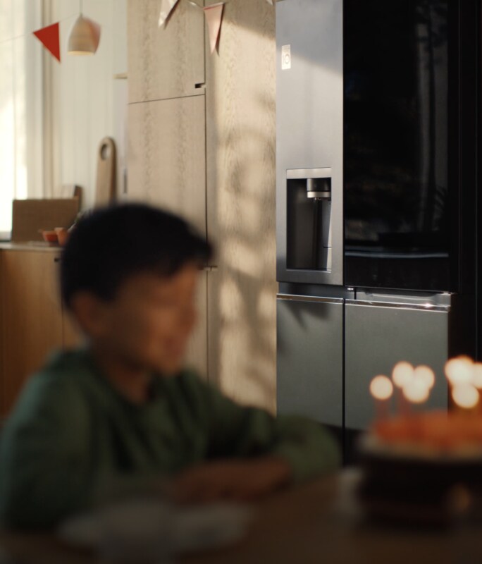 Das Gesicht des Kindes ist vor dem von Kerzen beleuchteten Kuchen nur schwach zu erkennen, im Hintergrund erkennt man deutlich den LG InstaView®-Kühlschrank.