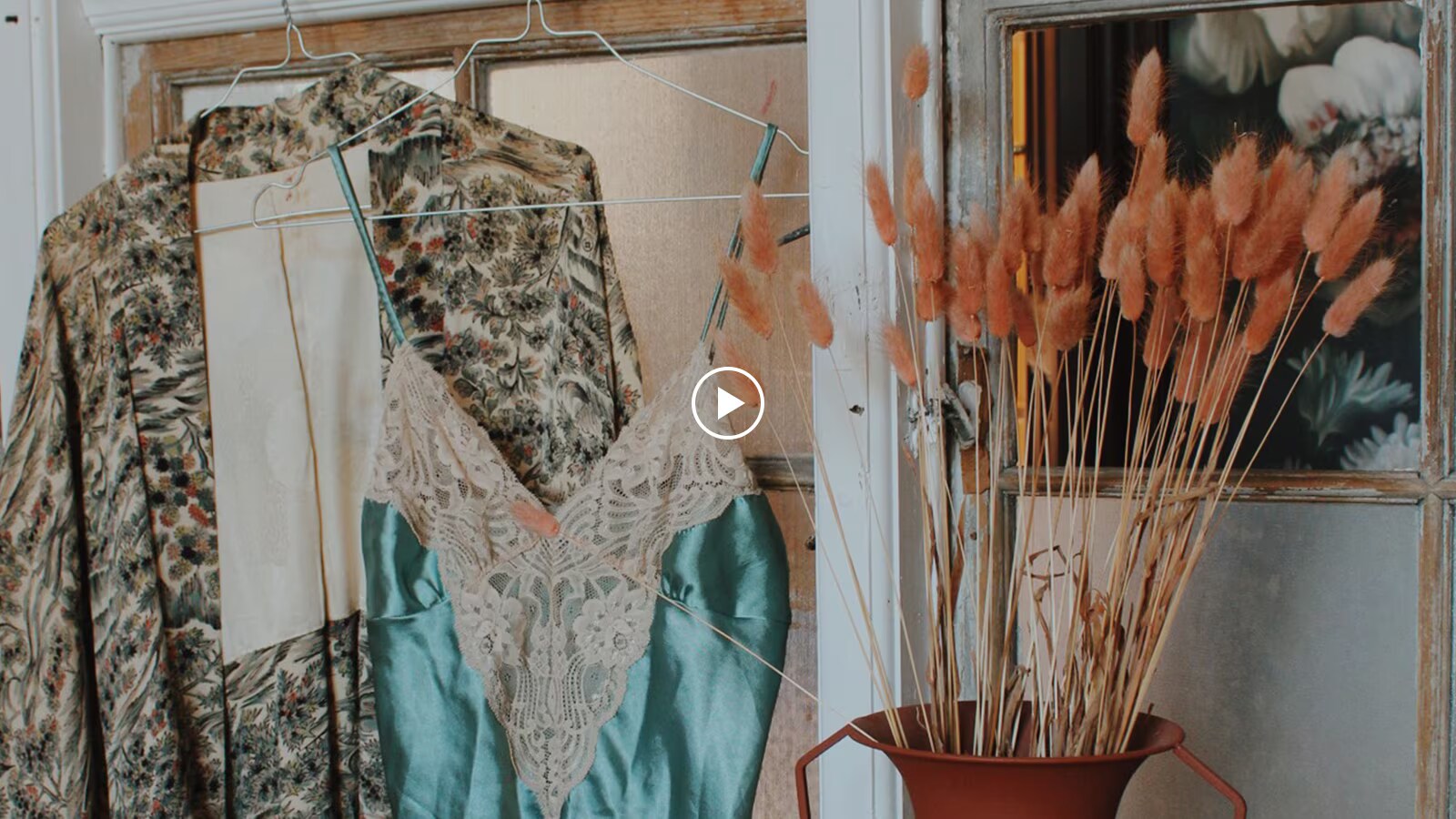 Et miniaturebillede af to hængende vintage tøj og en vase med baggrunden af vinduet.