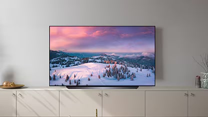 The LG OLED CS stands on a cabinet in a softly lit room with a snowy landscape on the screen.