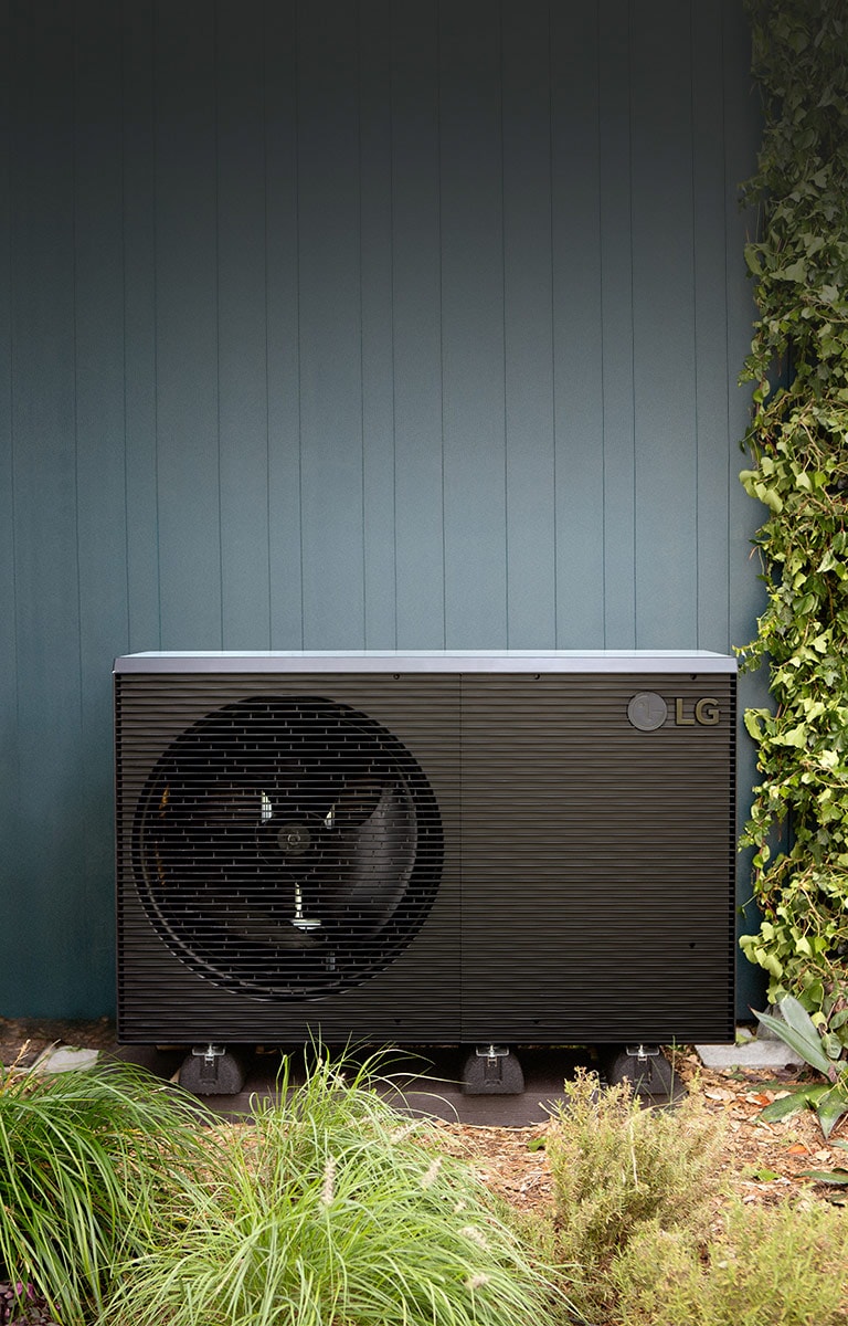 LG Air to Water Heat Pump THERMA V, black-colored outdoor unit is placed on the exterior wall of the house.	