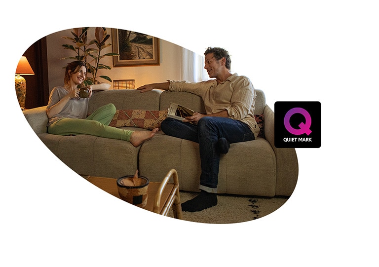 An adult woman and a man are sitting on a couch in the house and talking with a smile. There is a Quiet Mark certification logo next to the image.	