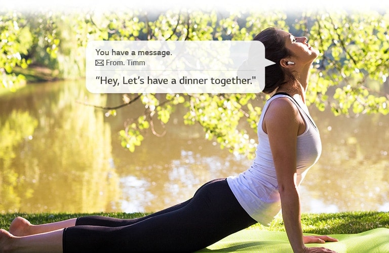 A woman is stretching and leaning down to touch the ground while she listens to a message that her earbuds read for her.